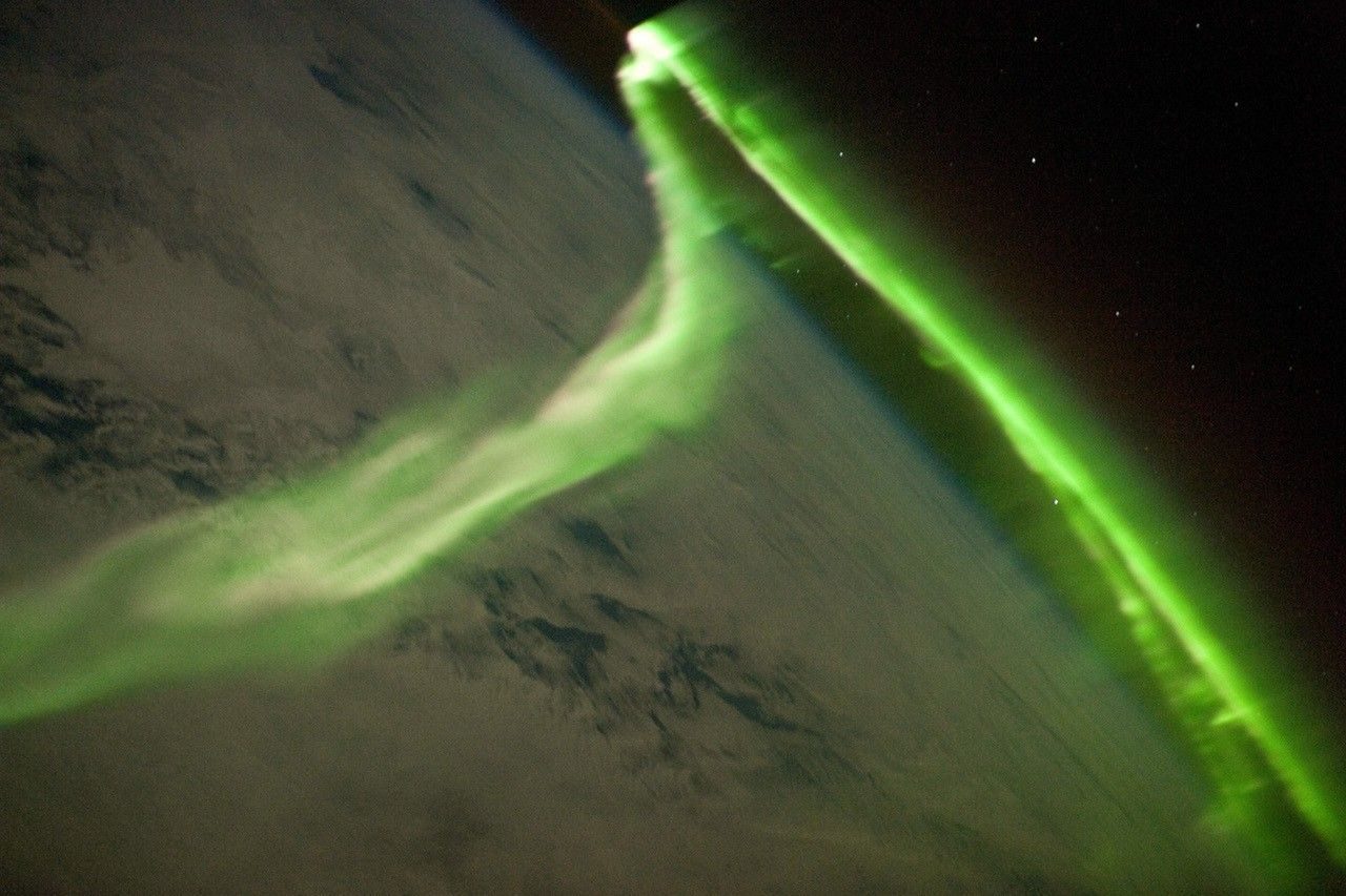 Un ruban vert d'aurore australe au-dessus d'une couche de nuages, vu depuis l'orbite